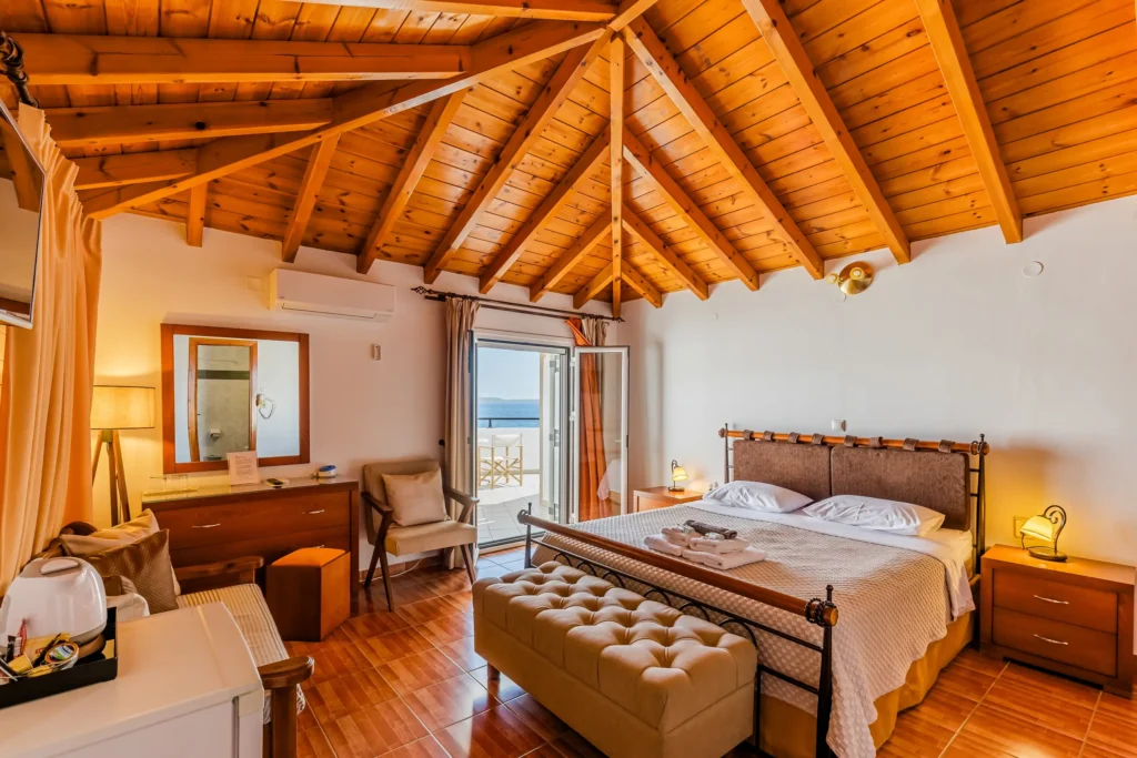 Hotel Filoxenia bedroom with a double bed, vaulted wooden ceiling, and a sea view balcony.