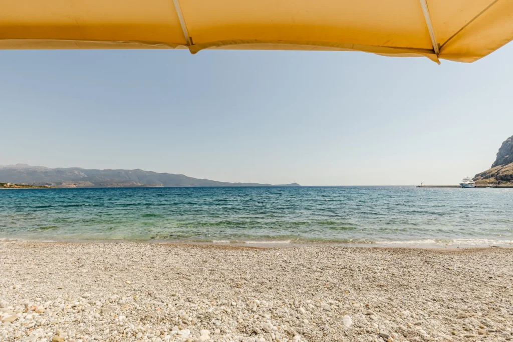 Pebble beach and blue sea view from Hotel Filoxenia in Monemvasia under a sun umbrella